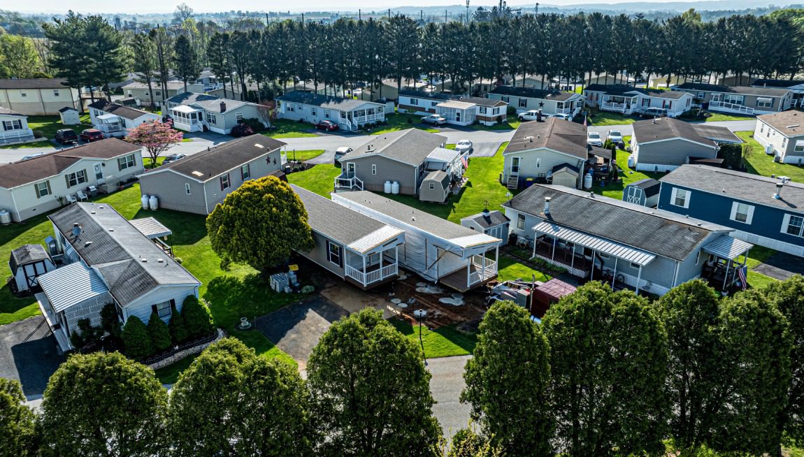 Aerial view of a mobile home park with multiple manufactured homes arranged in rows, surrounded by trees and green lawns.