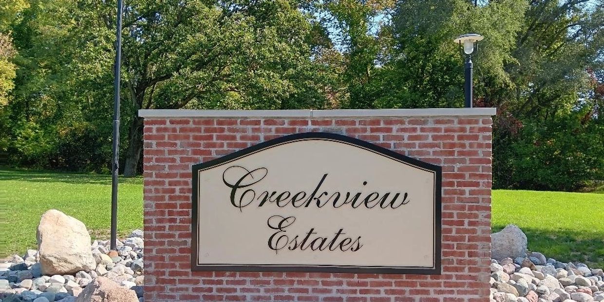 Signboard reading 'Creekview Estates' against a brick wall with trees in the background.