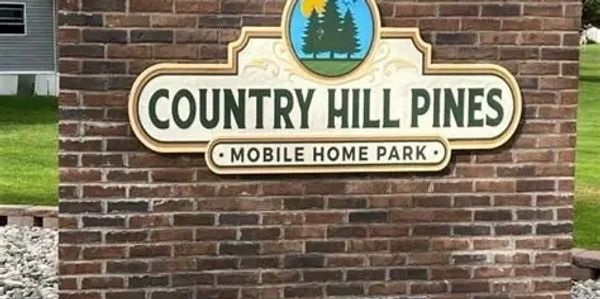 Sign for Country Hill Pines Mobile Home Park on a brick wall.