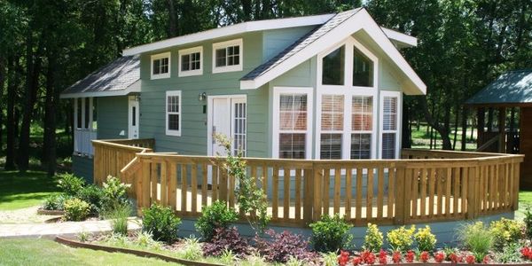 A charming green house with large windows and a wooden fence.
