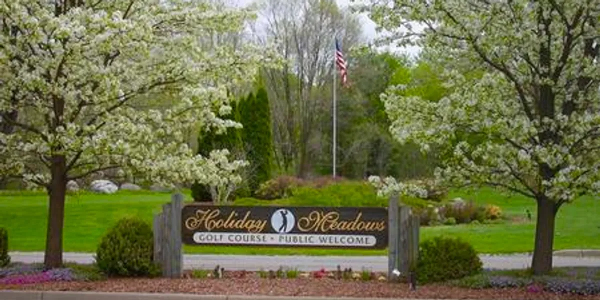 Entrance sign for Holiday Meadows residential community with blooming trees.