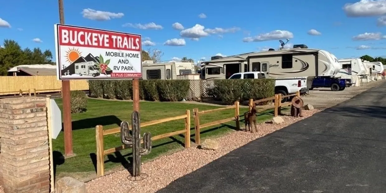 Entrance to a mobile home and RV park with wooden fencing and desert landscaping.