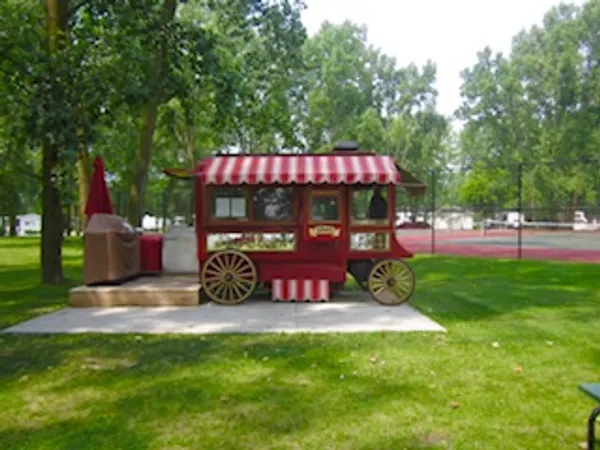 A wooden food cart with a striped canopy in a park.