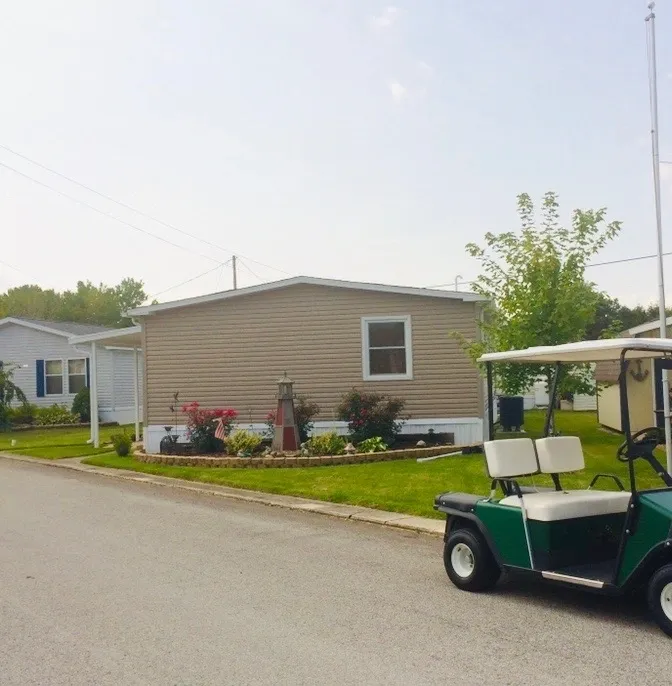 A golf cart parked on a street beside a beige mobile home.