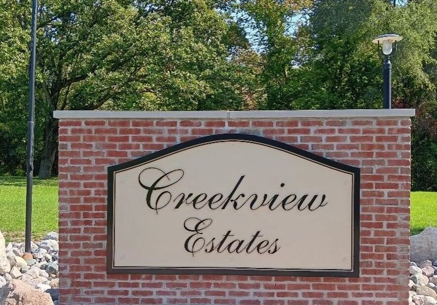Signboard reading 'Creekview Estates' against a brick wall with trees in the background.