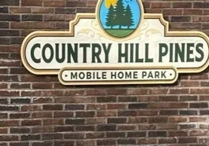 Sign for Country Hill Pines Mobile Home Park on a brick wall.
