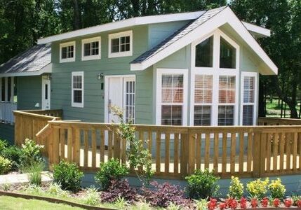 A charming green house with large windows and a wooden fence.