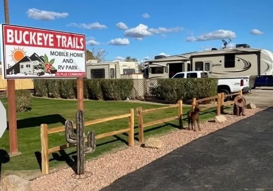 Entrance to a mobile home and RV park with wooden fencing and desert landscaping.